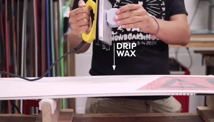 Move the iron smoothly and steadily across the snowboard base, applying wax in a zigzag pattern, ensuring even coverage. Always keep the iron moving to avoid overheating the base. Pay special attention to the edges.