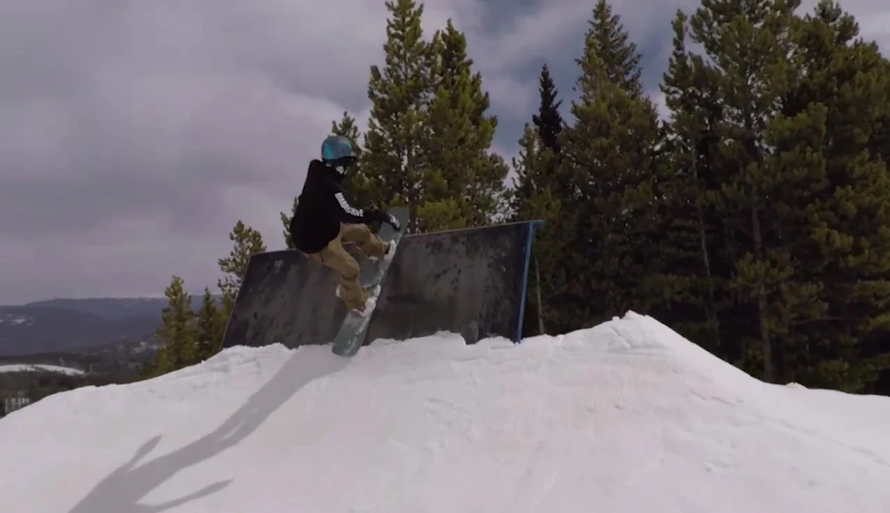 The snowboarder performing a press on the rocker board in the terrain park.