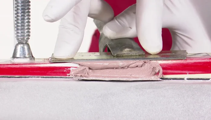 Use a petroleum jelly-coated steel scraper to further flatten and level the surface. Clamp and press down. Wait for curing.