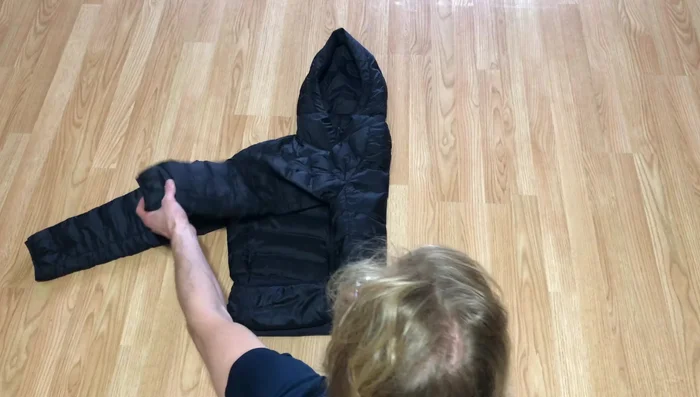 Fold the other side over the previous fold, and fold the sleeve back across and up as well, keeping it in line with the coat.